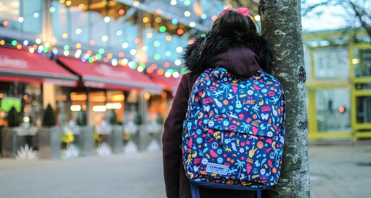 Schulreform_Unsplash_Jamie-O_Sullivan_1200. Ein Kind mit Schulranzen blickt auf ein Gebäude, an dem viele Lichter blinken.